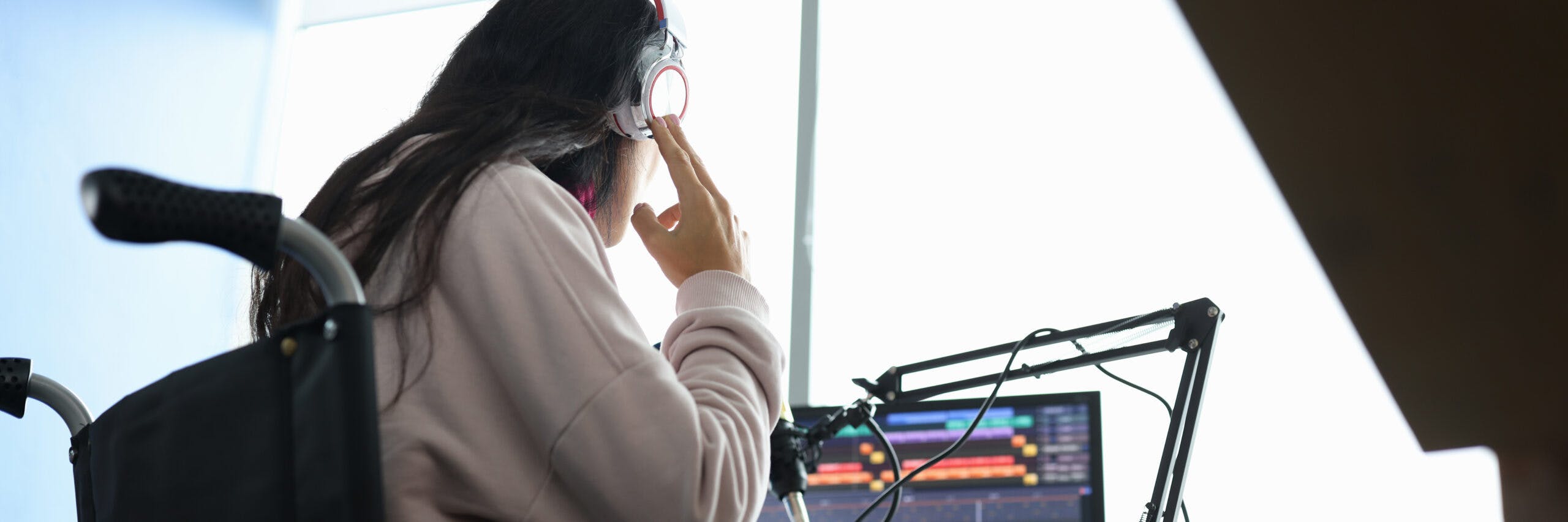 Woman in wheelchair with headphones in front of microphone and computer